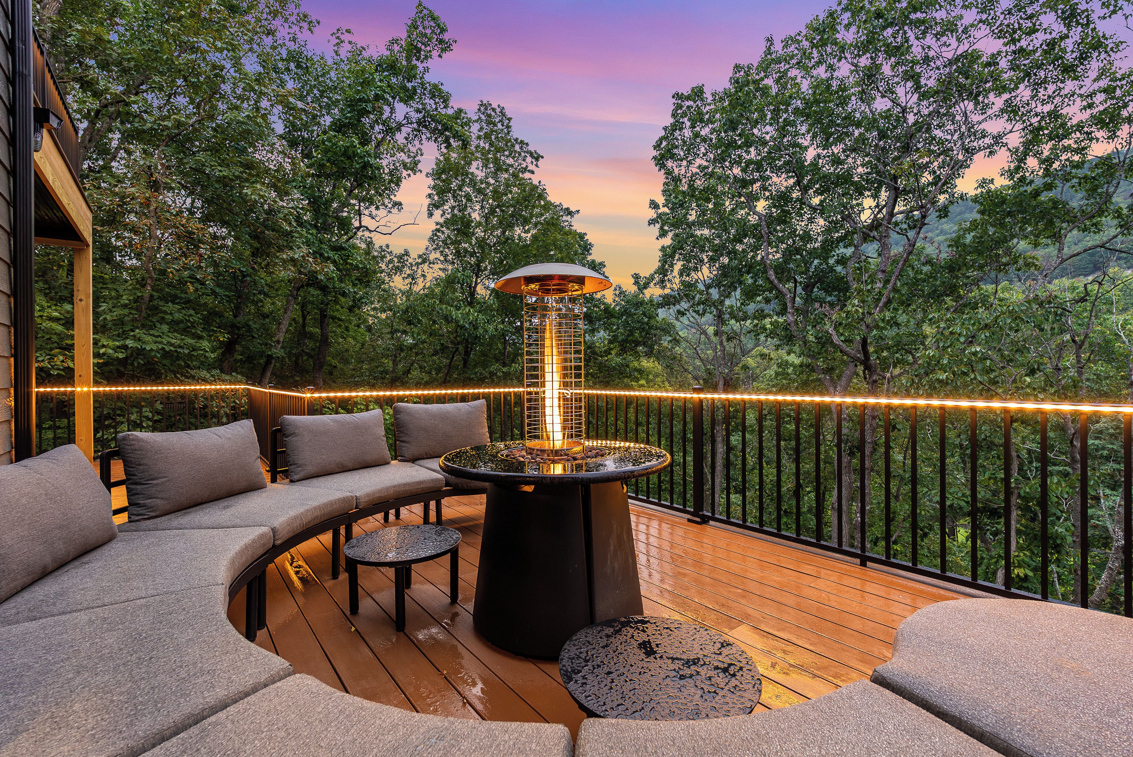 An outdoor deck with a fire feature, seating, and a view of the surrounding forest.