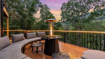 An outdoor deck with a fire feature, seating, and a view of the surrounding forest.