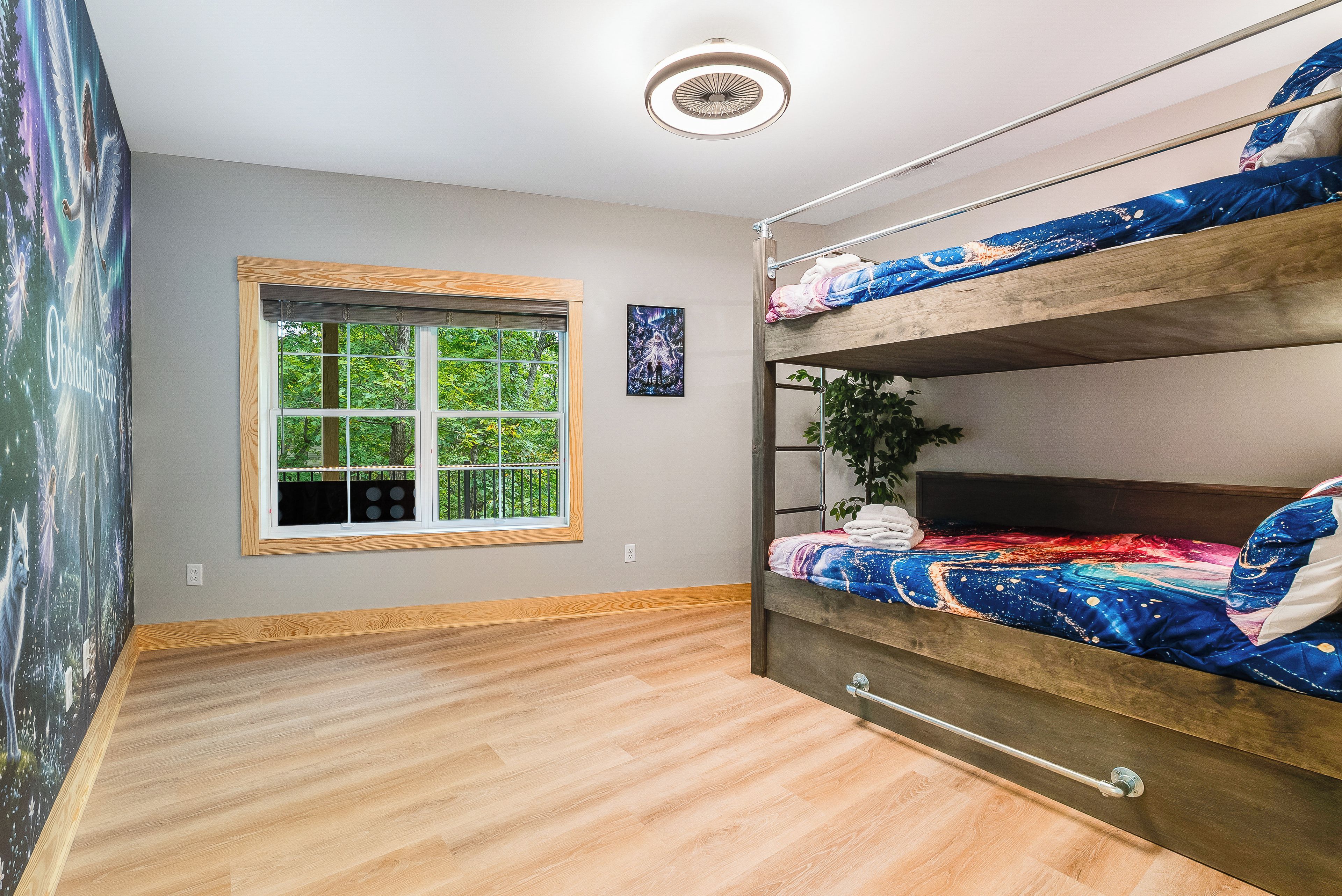 A room with a bunk bed, a window with a view of greenery, a ceiling light, and a wall with a framed picture.