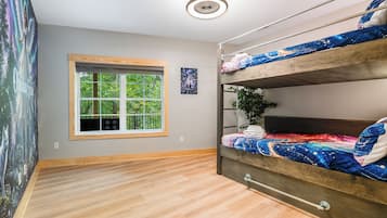 A room with a bunk bed, a window with a view of greenery, a ceiling light, and a wall with a framed picture.