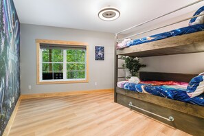 Una habitación con literas, una ventana que da a zonas verdes, una lámpara en el techo y una pared decorada con un cuadro.
