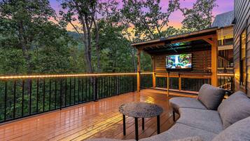 A wooden deck with outdoor seating and a TV screen.