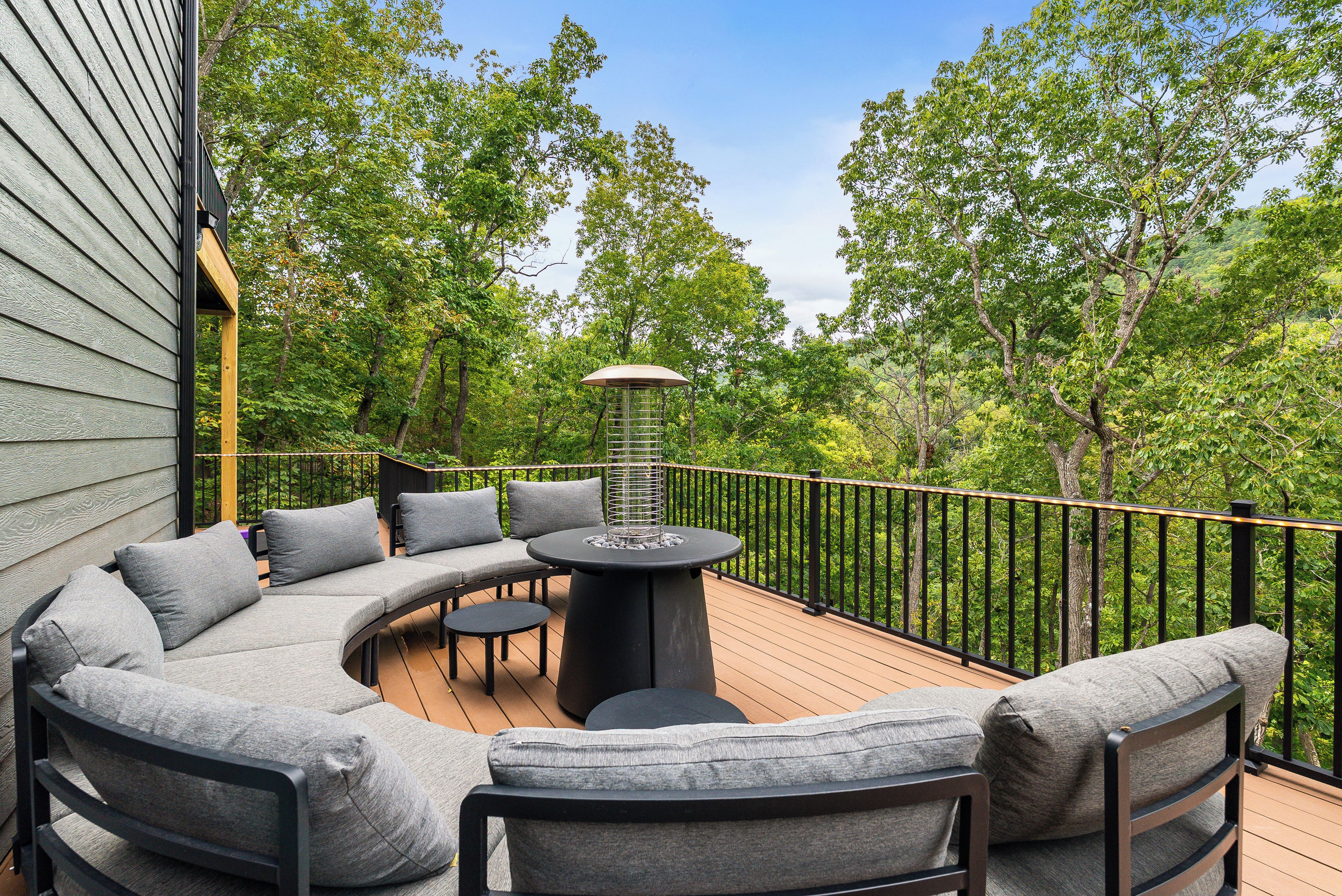A deck with a curved sofa, a round table, and a metal railing.