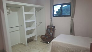 Una habitación con un armario blanco, una silla estampada y un ventanal.