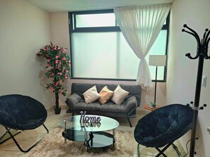 A living room with a grey sofa, two black chairs, a glass coffee table, a potted plant, and a window with curtains. - A1 Cuadra Historic Center New Apartment 2 Bedrooms 24/7 Parking (La Piedad de Cabadas)