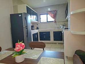 Una cocina compacta con refrigerador, armarios y un ventanal con cortinas.