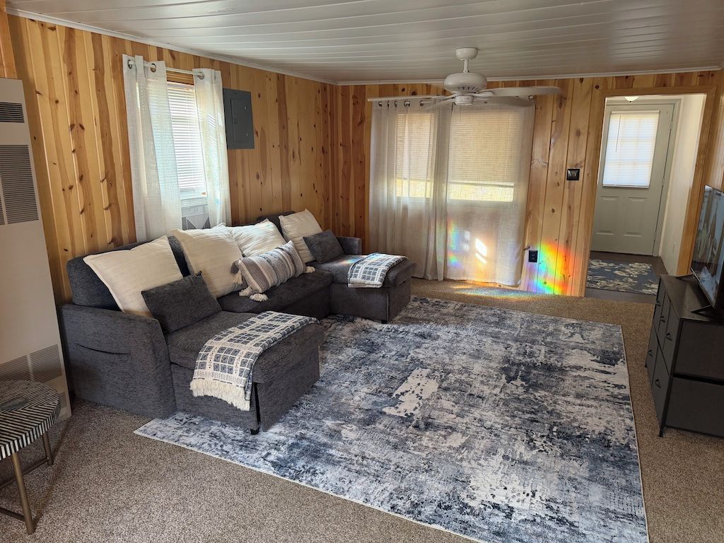 Une pièce avec un canapé d’angle, un tapis à motifs et un ventilateur de plafond.