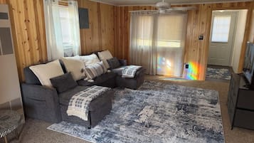 Une pièce avec un canapé d’angle, un tapis à motifs et un ventilateur de plafond.