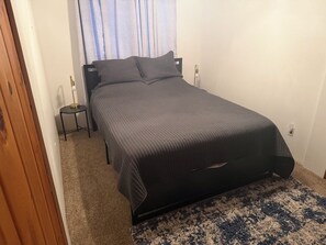 Un dormitorio con una cama, una mesita de noche, una lámpara y un ventanal con cortinas.