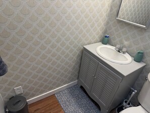 Un baño con papel tapiz estampado, un lavamanos con un espejo encima y un inodoro.