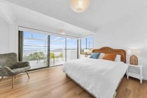 A modern bedroom with a large bed, a chair, and a balcony with a view. - Pambula Little Beach House (Pambula Beach)
