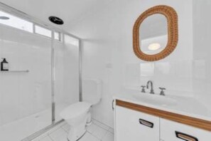 A bathroom with a glass shower enclosure, a toilet, and a vanity with a mirror. - Pambula Little Beach House (Pambula Beach)