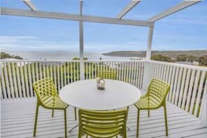 A covered outdoor seating area with a round table and chairs, surrounded by white railings. - Pambula Little Beach House (Pambula Beach)