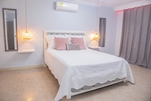 A bedroom with a bed, bedside tables, a hanging light fixture, and a window with curtains. - Big House with Yard Near the Beach - Daily Cleaning (Cartagena de Indias)