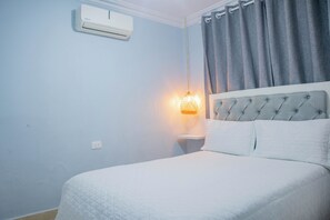 Ein Schlafzimmer mit einem Bett, einem Nachttisch, einer Klimaanlage und einer Wandlampe.