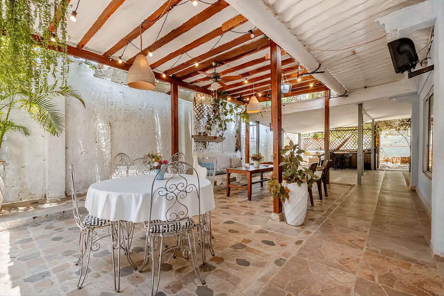 An indoor patio area with a stone floor, metal chairs, a round table with a white tablecloth, and hanging plants.