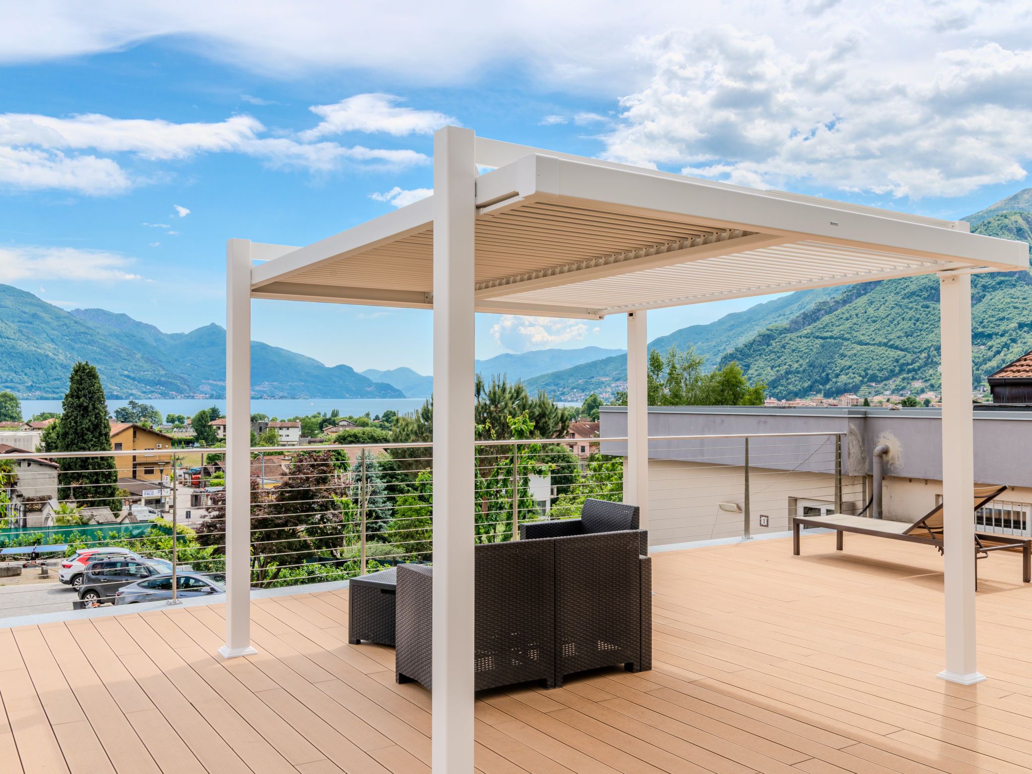 A covered outdoor area with a wooden deck, wicker furniture, and a view of a lake and mountains.