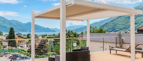 A covered outdoor area with a wooden deck, wicker furniture, and a view of a lake and mountains.