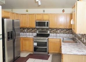 A kitchen with wooden cabinets, a stainless steel refrigerator, a microwave, an oven, and a tiled backsplash. - 3-bedroom house in fantastic East Tucson with cool AC and comfort (Tucson)