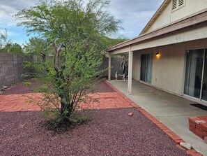 A covered patio area with a small tree, a brick pathway, and a building with a garage door. - 3-bedroom house in fantastic East Tucson with cool AC and comfort (Tucson)