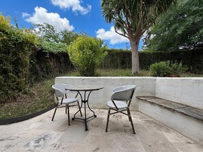 An outdoor seating area with a table and two chairs, surrounded by a low wall and dense foliage. - XIXTABERRI - CAMBO-LES-BAINS (CAMBO-LES-BAINS)