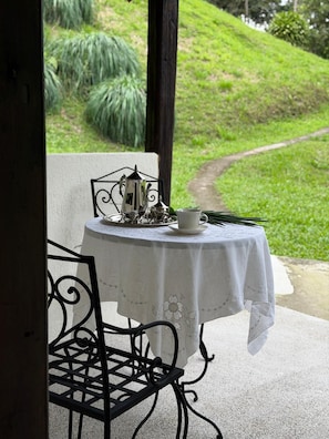 Una mesa servida con tetera, taza y platillo, con vista a un área cubierta de césped y un sendero.