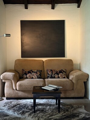 A living room with a sofa, two pillows, a coffee table, a rug, and a large dark artwork on the wall. - Casa Unai Boutique Lodge  (Nanegalito)