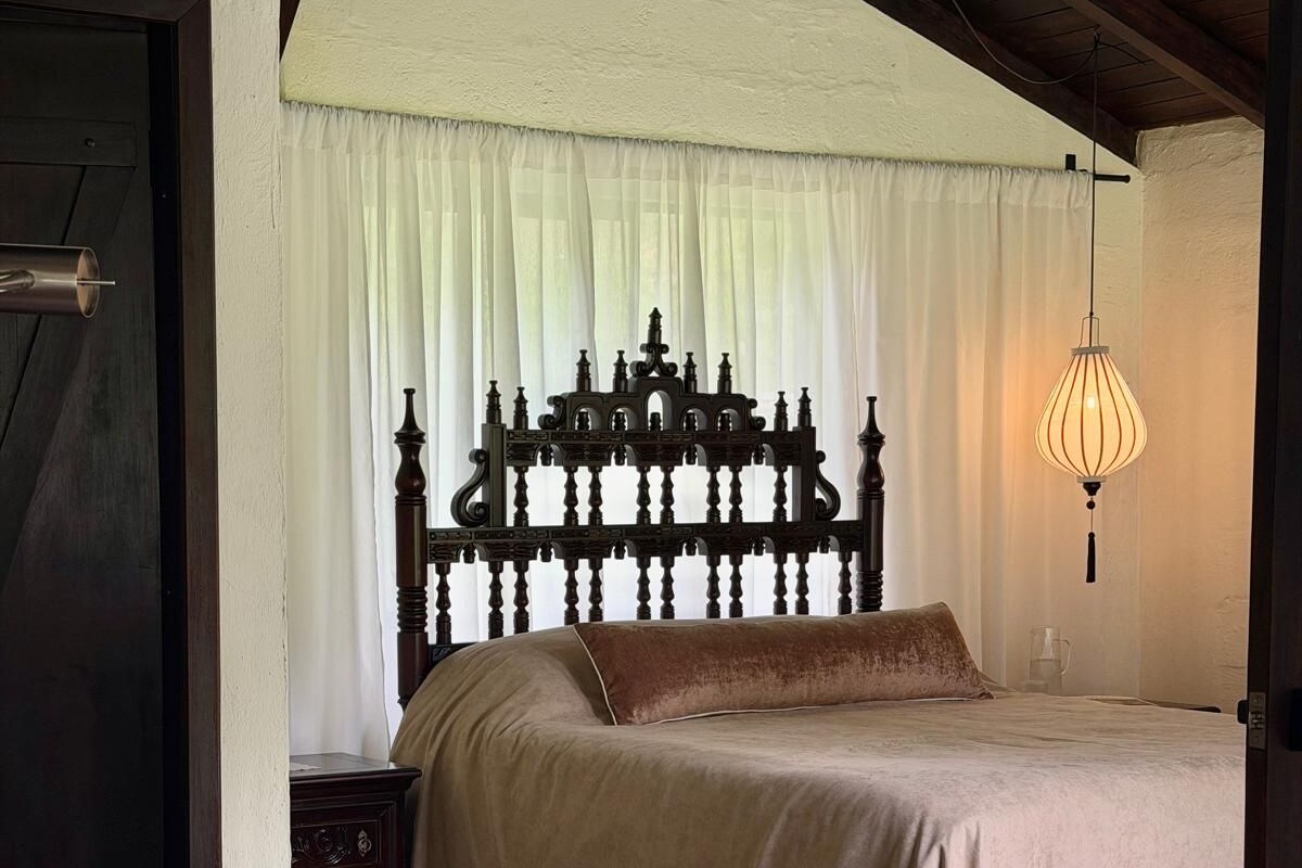 A bedroom with a large bed, a wooden headboard, a bedside table, and a hanging light fixture.