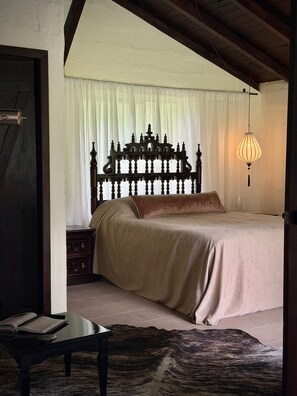 A bedroom with a large bed, a wooden headboard, a bedside table, and a hanging light fixture. - Casa Unai Boutique Lodge  (Nanegalito)