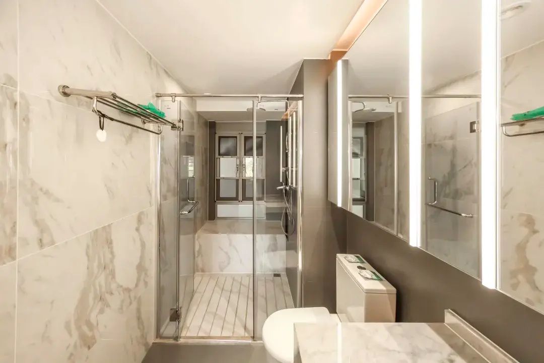 A modern bathroom with a glass-enclosed shower, a toilet, and a large mirror.