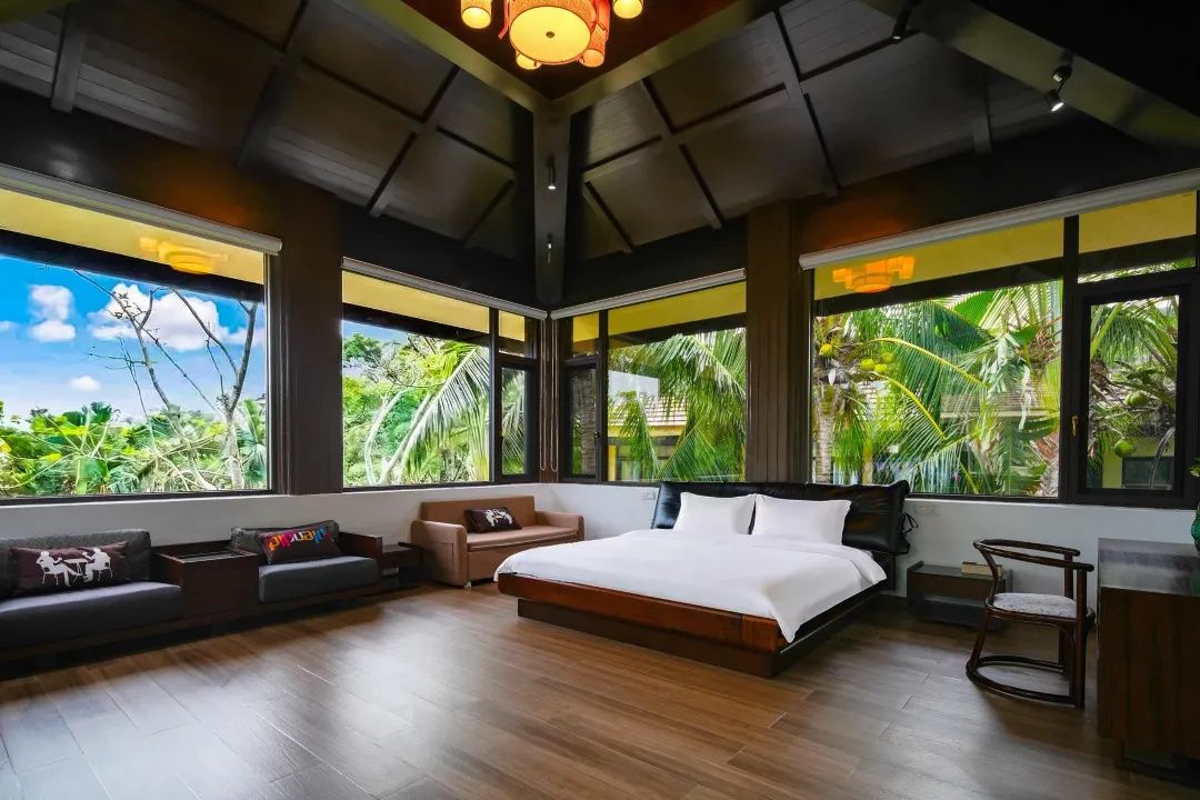 Quarto com cama grande, sofá e poltrona, com amplas janelas que dão para o verde.