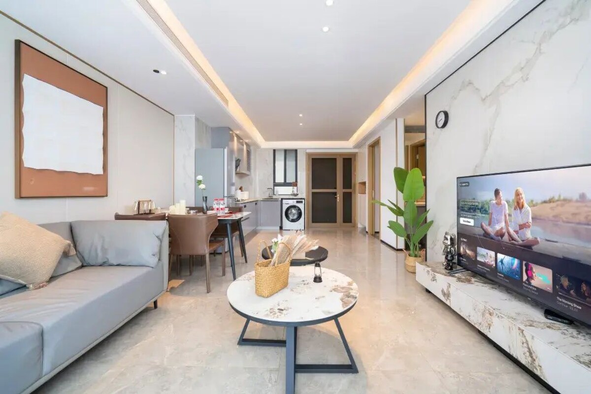 Ein modernes Wohnzimmer mit einer Couch, einem runden Couchtisch, einem Fernseher und einer Küchenzeile im Hintergrund.