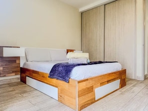Quarto com estrutura de cama de madeira, roupa de cama branca e um guarda-roupa grande.