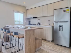 A modern kitchen with a central island, bar stools, a stainless steel refrigerator, and a window providing natural light. - Modern Apartment with Private Jacuzzi and Rooftop Infinity Pool • 5-Minute Walk to the Beach (Cartagena de Indias)