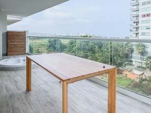A balcony with a wooden table, a glass railing, and a city view. - Modern Apartment with Private Jacuzzi and Rooftop Infinity Pool • 5-Minute Walk to the Beach (Cartagena de Indias)