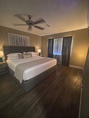 Un dormitorio con una cama grande, un ventilador de techo y una ventana con cortinas.