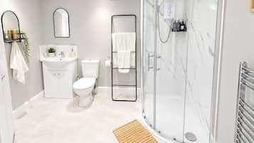 A modern bathroom with a glass-enclosed shower, a white toilet, a sink with a mirror, and a wooden mat.