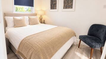 Quarto com cama, uma cadeira, janela com cortina e dois quadros pendurados na parede.