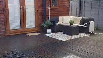 A wooden cabin with a patio area featuring a sofa set, a coffee table, and a small plant.