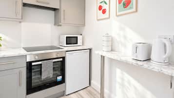 Una cuina moderna amb forn integrat, microones i rentaplats petit. Hi ha dos quadres al mur, una torradora i una bullidora a la tauleta.
