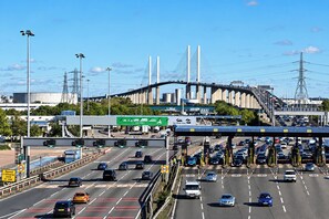 Eine belebte Mautstelle mit mehreren Fahrspuren und einer Brücke im Hintergrund.