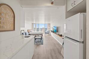 Quarto de hotel moderno com uma cama grande, área de cozinha e vista para a paisagem urbana.