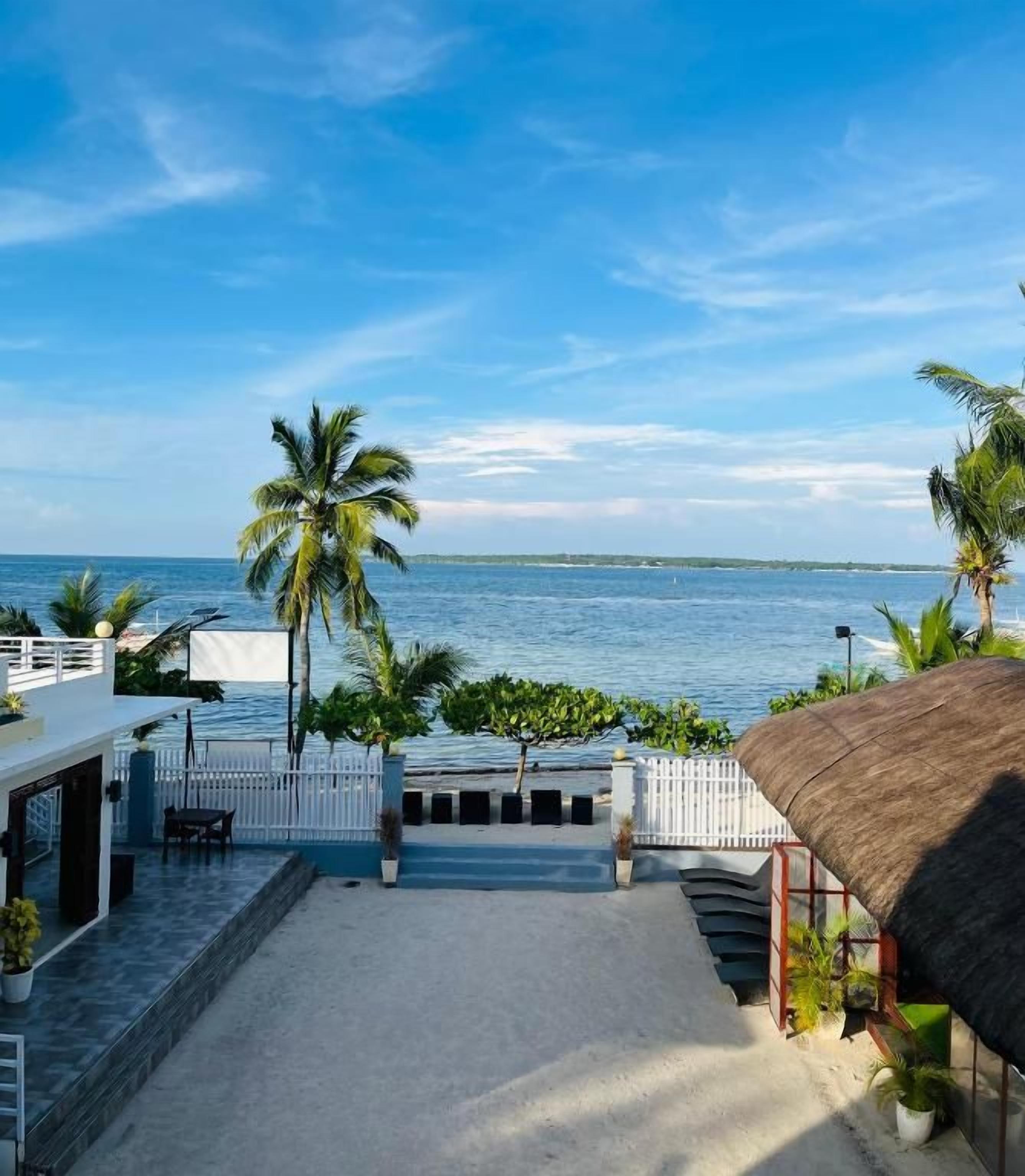 A beachfront property with a patio, palm trees, and a view of the sea.