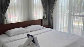 A hotel room with a large bed, curtains, an air conditioning unit, and a view of the outdoors.