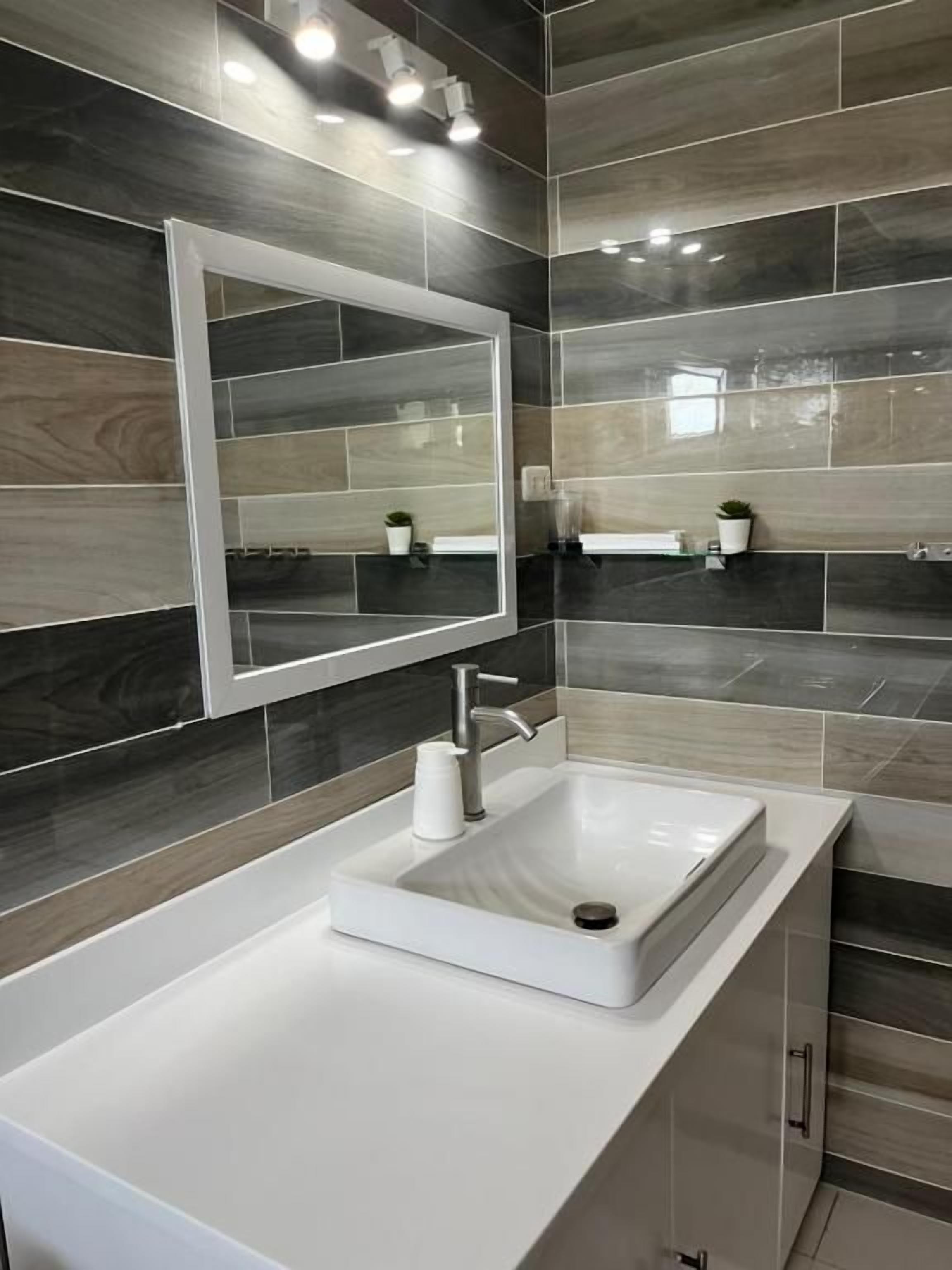 Un baño con lavamanos blanco, un espejo y baldosas gris oscuro.