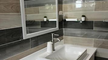 Un baño con lavamanos blanco, un espejo y baldosas gris oscuro.