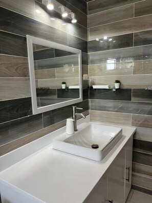 A bathroom with a white sink, a mirror, and dark grey tiles. - Maykenn Beach Resort (Bantayan)