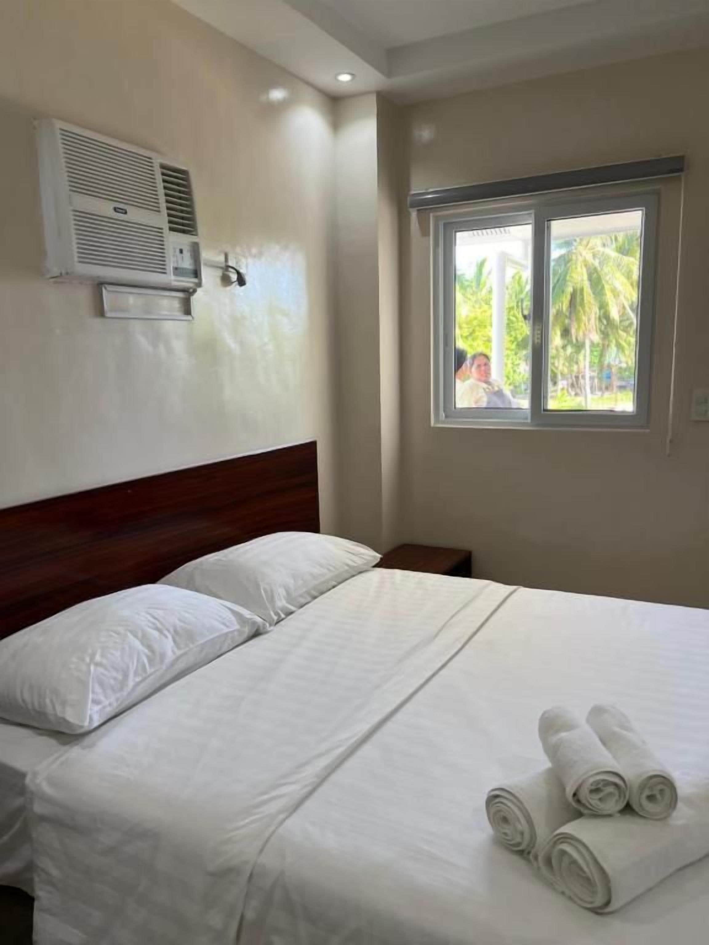 Habitación de hotel con cama, almohadas, ventana con vistas y aire acondicionado.