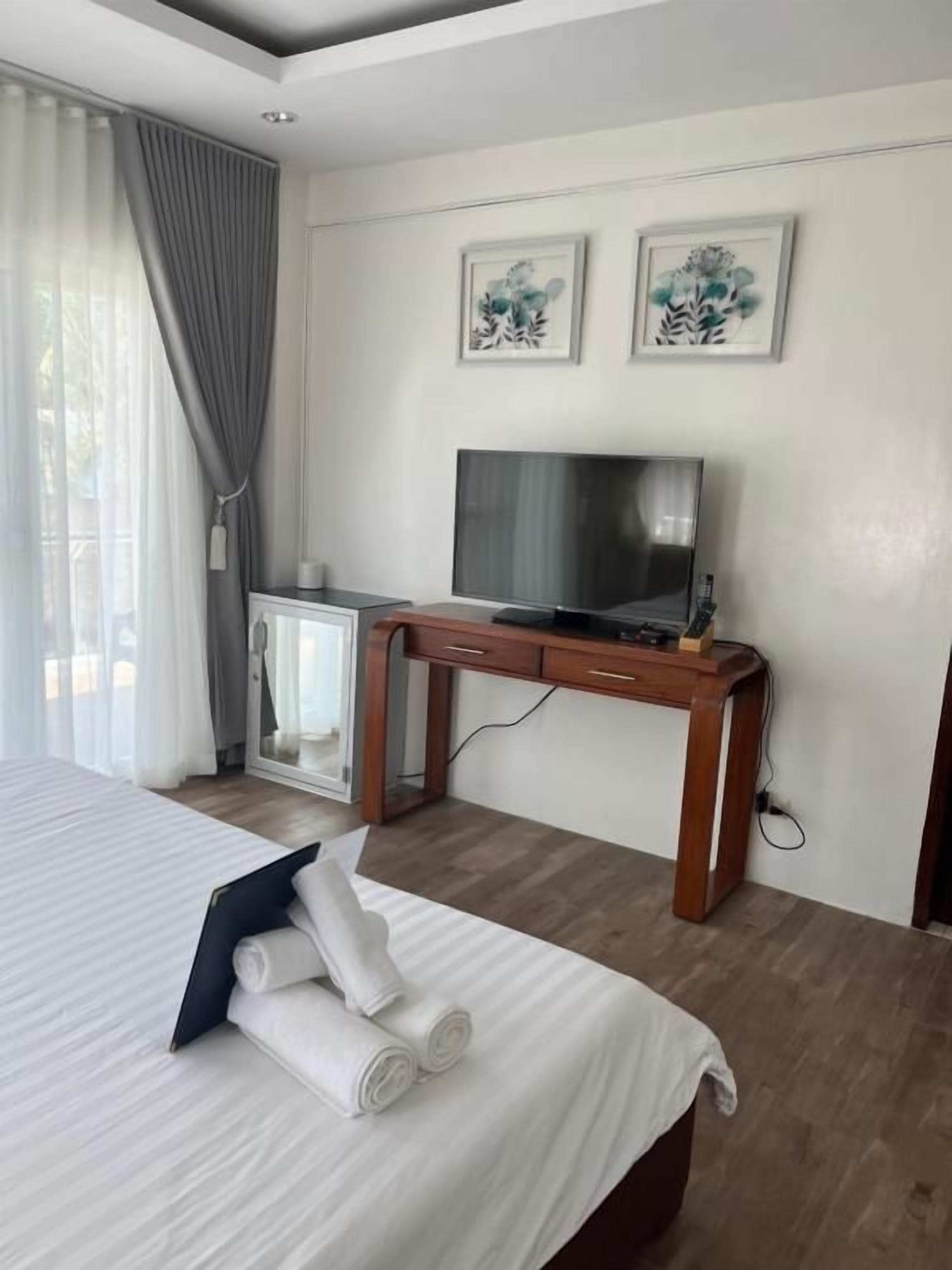 A hotel room with a bed, a desk with a television, and two framed pictures on the wall.