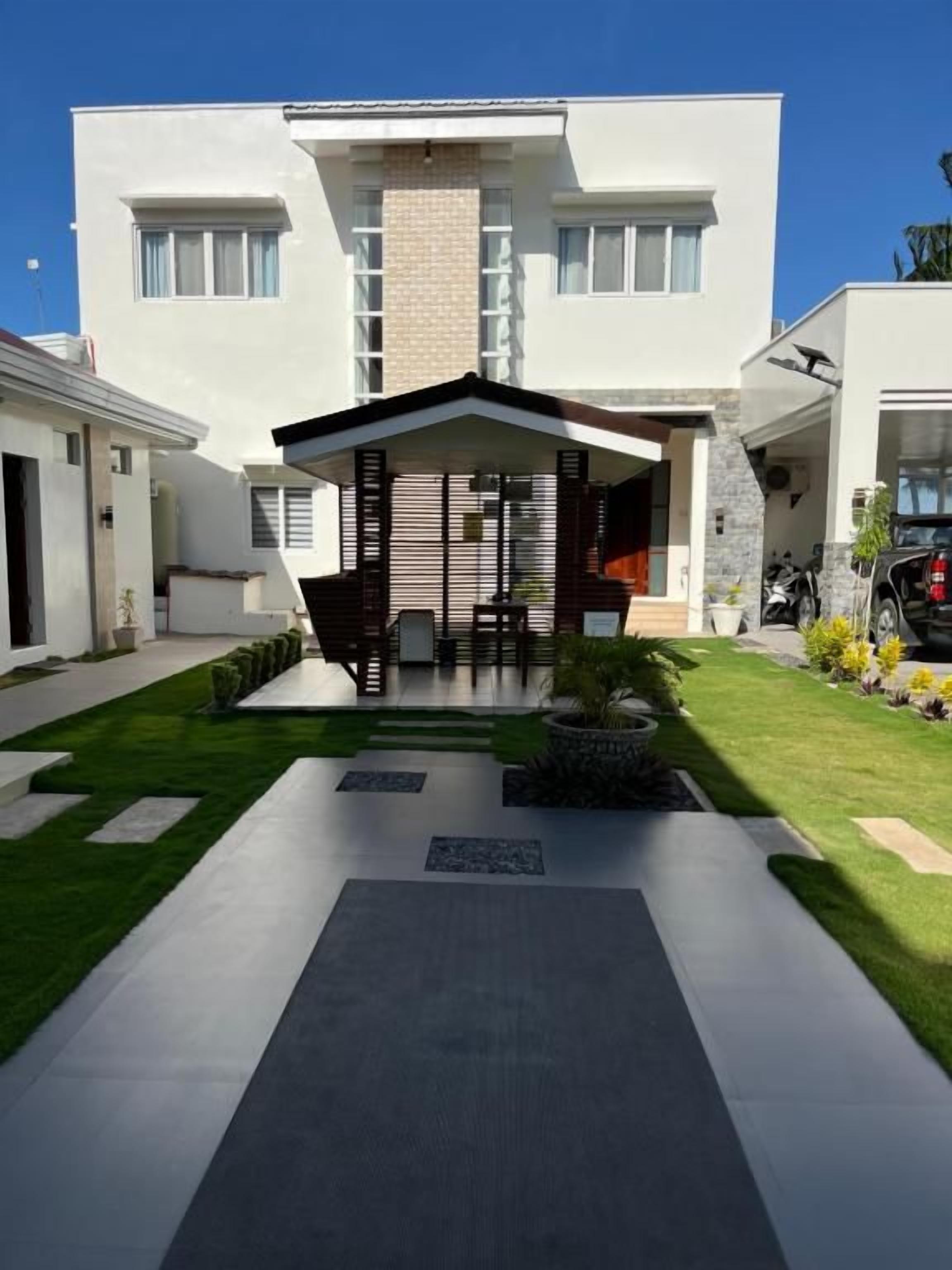 A modern two-story house with a covered patio, a driveway, and a well-maintained lawn.